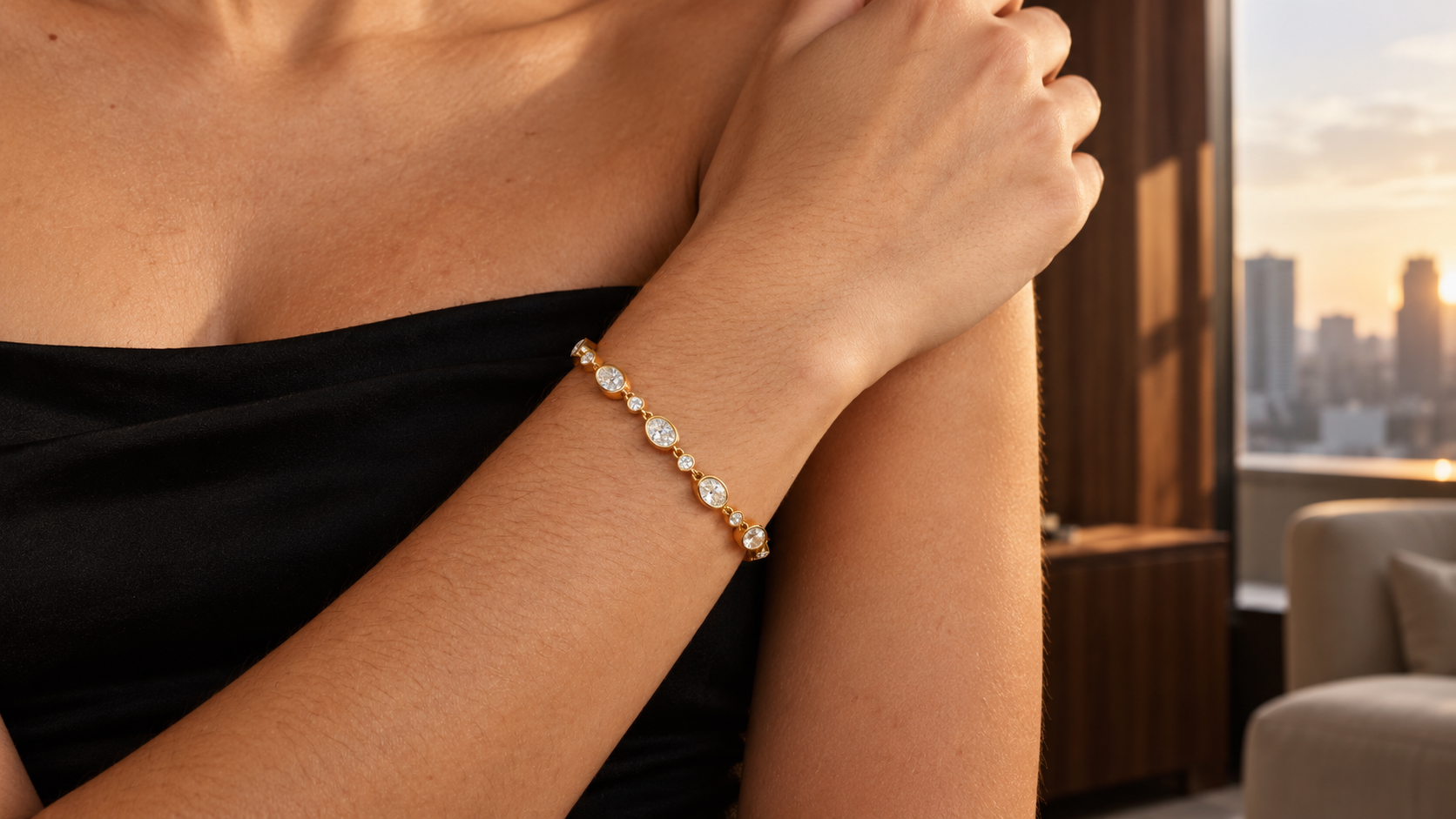 Aura Bracelet in gold worn at the wrist with black clothing in warm window light.